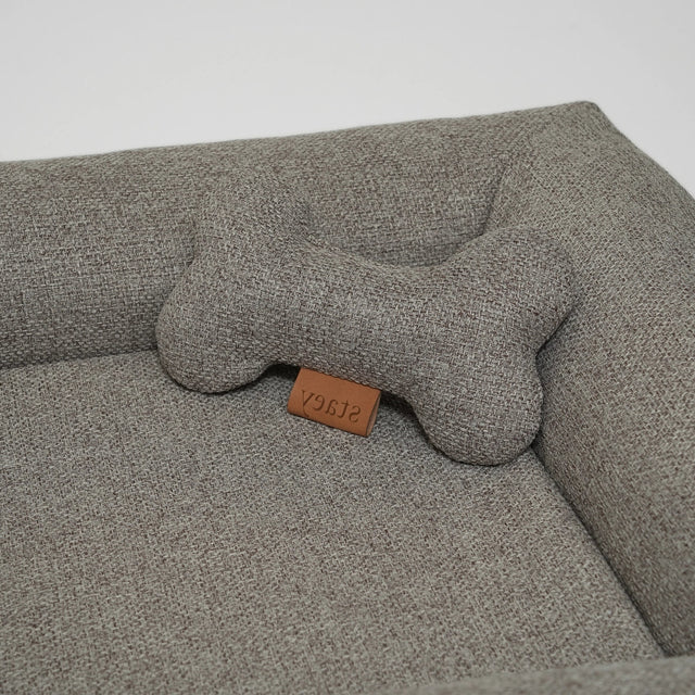 Jouet pour chien en tissu gris corde, forme os, posé sur panier pour chien